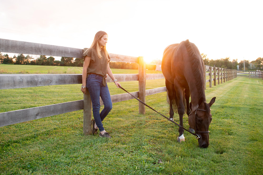 Maddy Keyes leans against fence while Classic Circle grazes